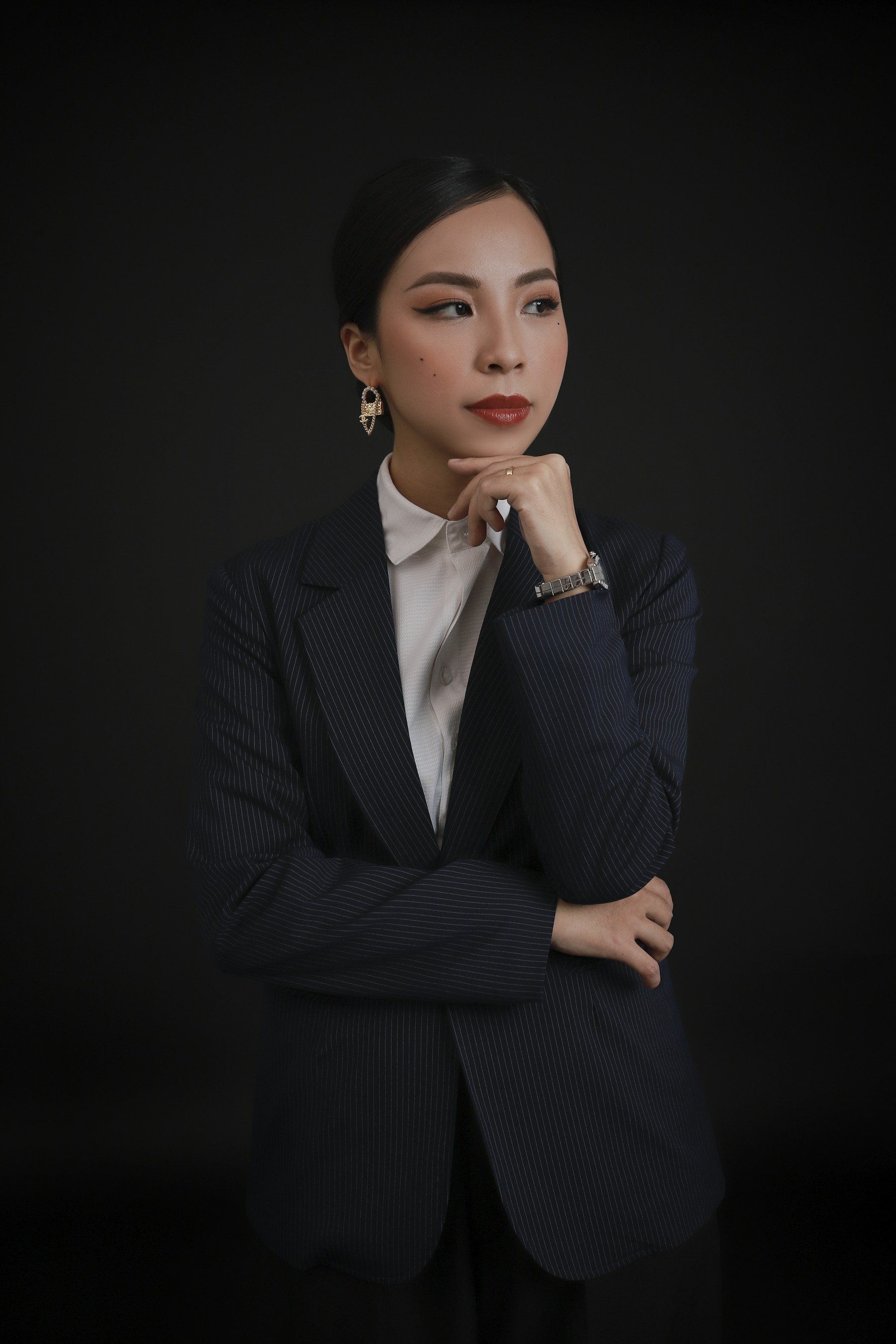 华人女模特身着深色细条纹西装，站在黑色背景前